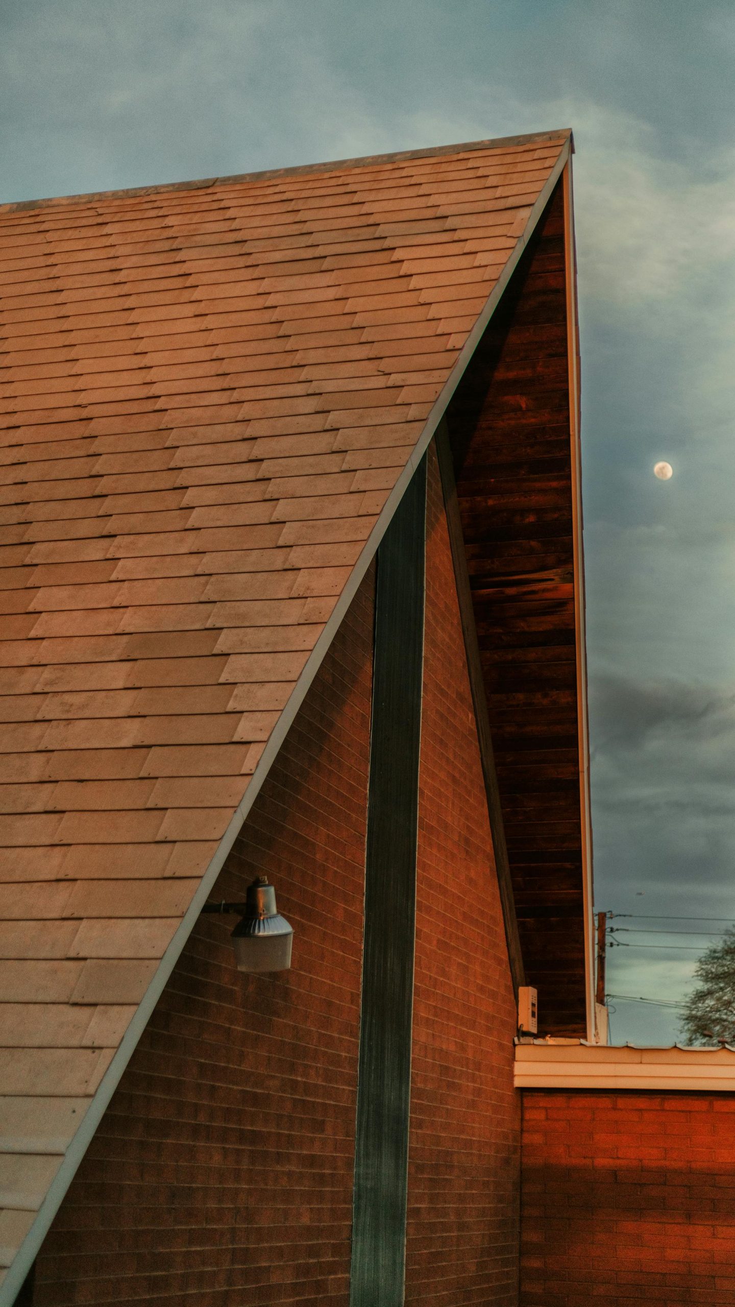 A-frame house roof under twilight sky with moon. Architectural detail captured in warm evening light.